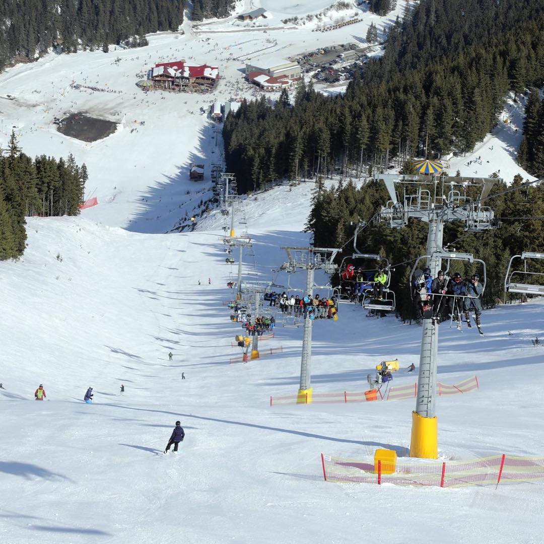 Вид на горнолыжный спуск: с одной стороры спускаются люди на лыжах и сноуборде, на другой кресельный подъемник