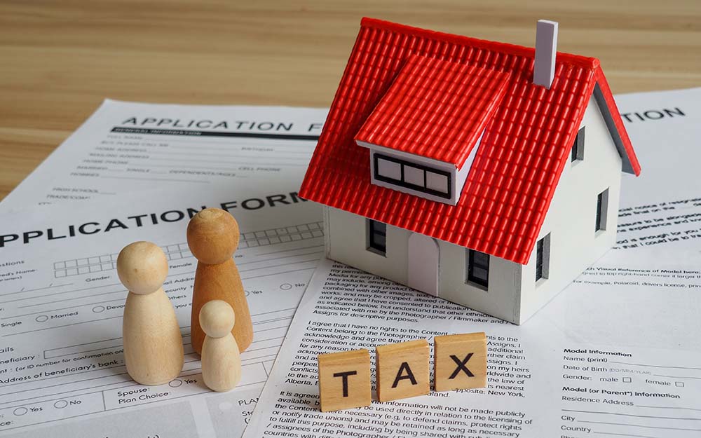 Модель дома с красной крышей с деревянными кубиками TAX и документами иллюстрирующая оптимизацию налогообложения продажи недвижимости для граждан ЕС