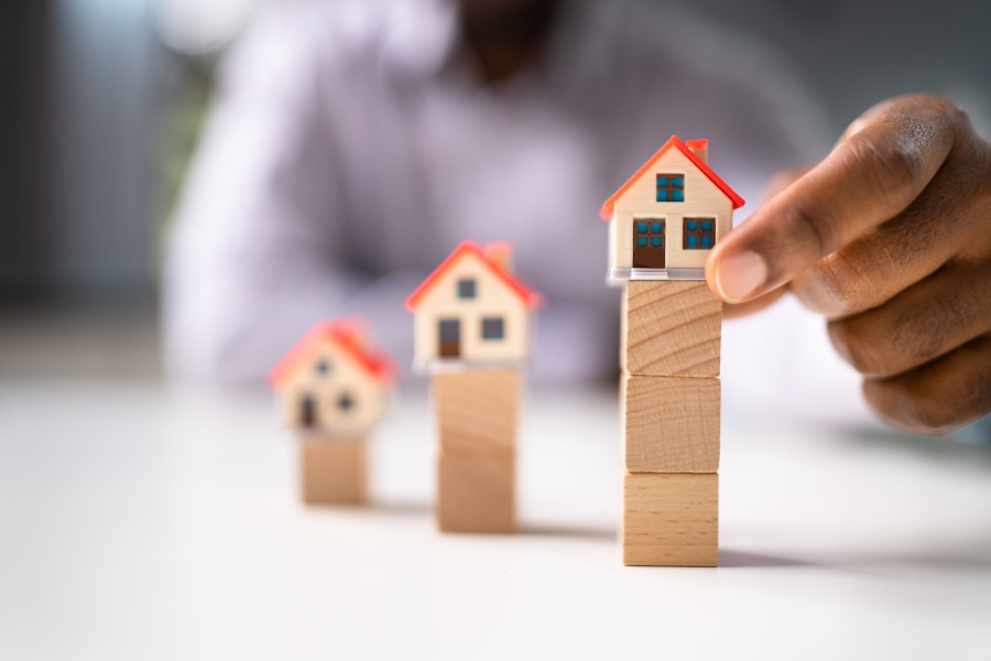 Рука выстраивает модели домов на деревянных блоках, показывая градацию цен и риски рынка котлована в Болгарии.